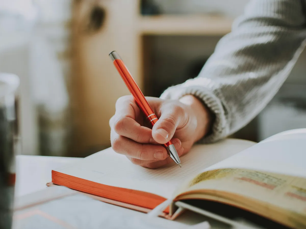 A hand writing in a notebook with a red pen