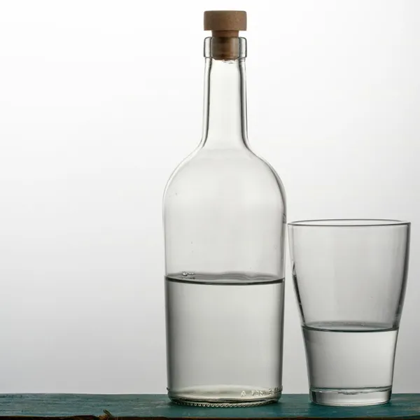 A glass bottle of water next to a glass