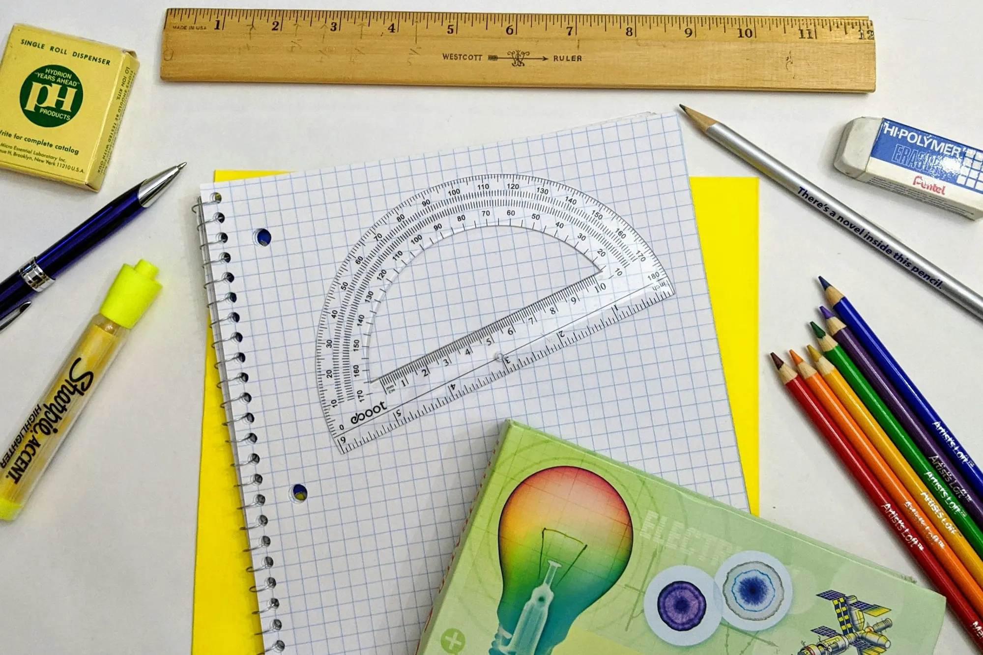 A bright desk with a notebook, coloured pencils, a book and a ruler